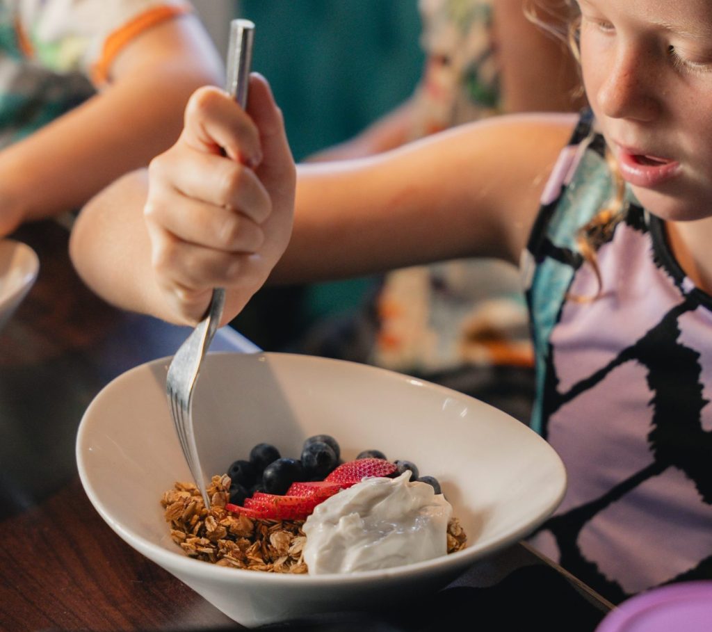 Girl enjoying breakfast at a Bite Club restaurant with her siblings dining together in the background.
