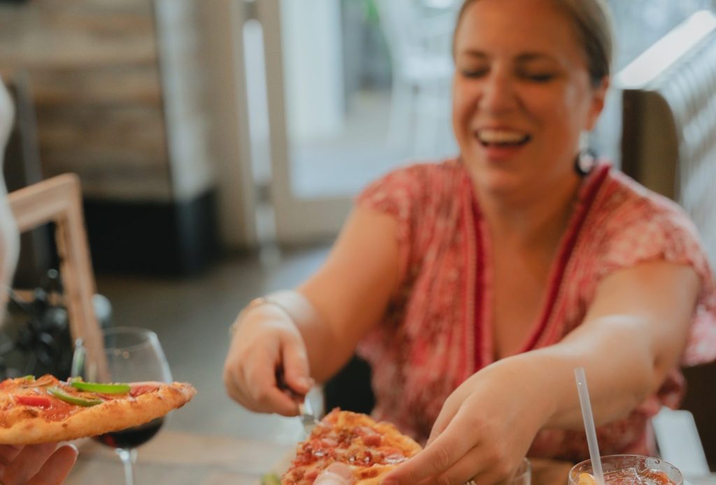 woman smiling and sharing pizza at a restaurant table