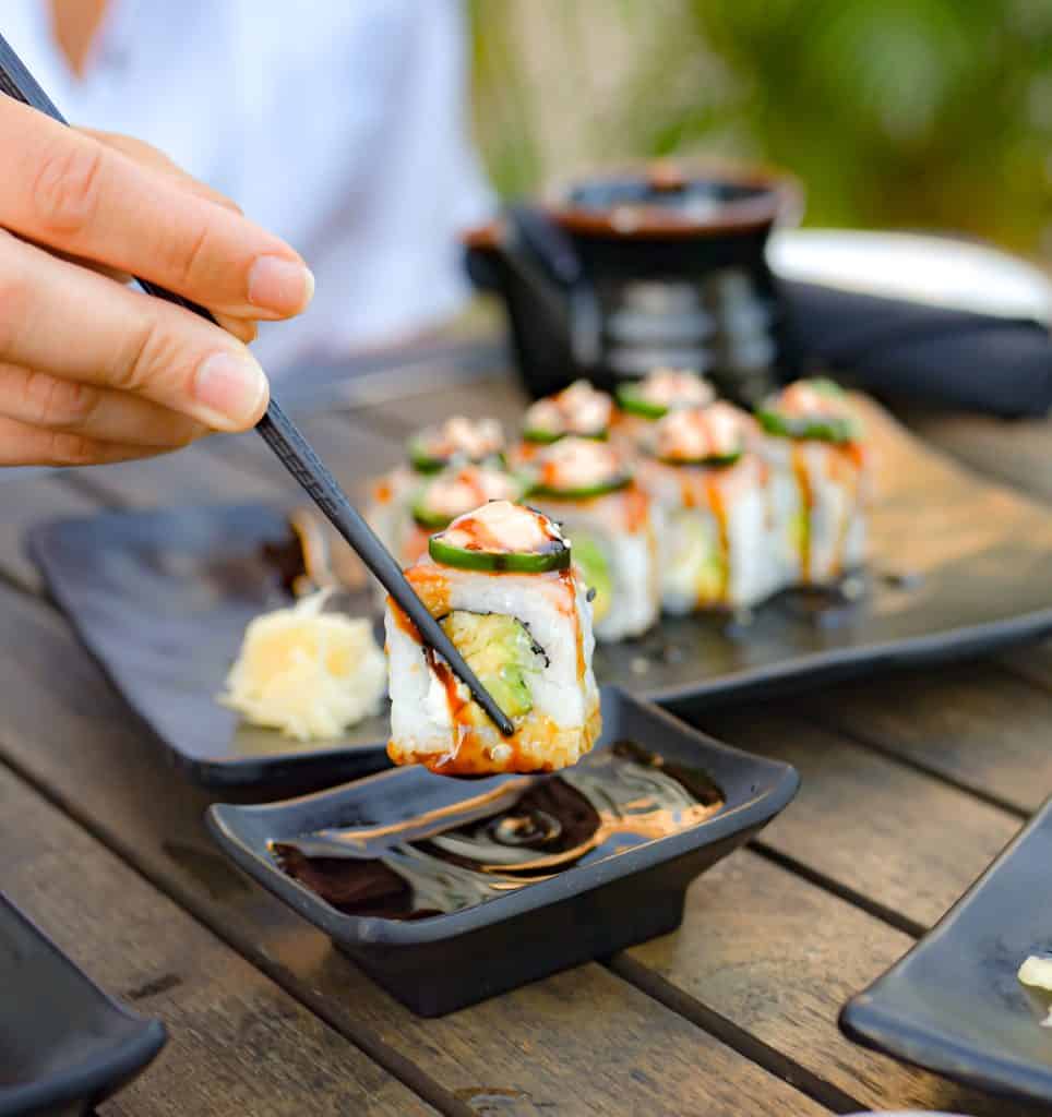 Sushi being picked up with black chopsticks at an outdoor dining table